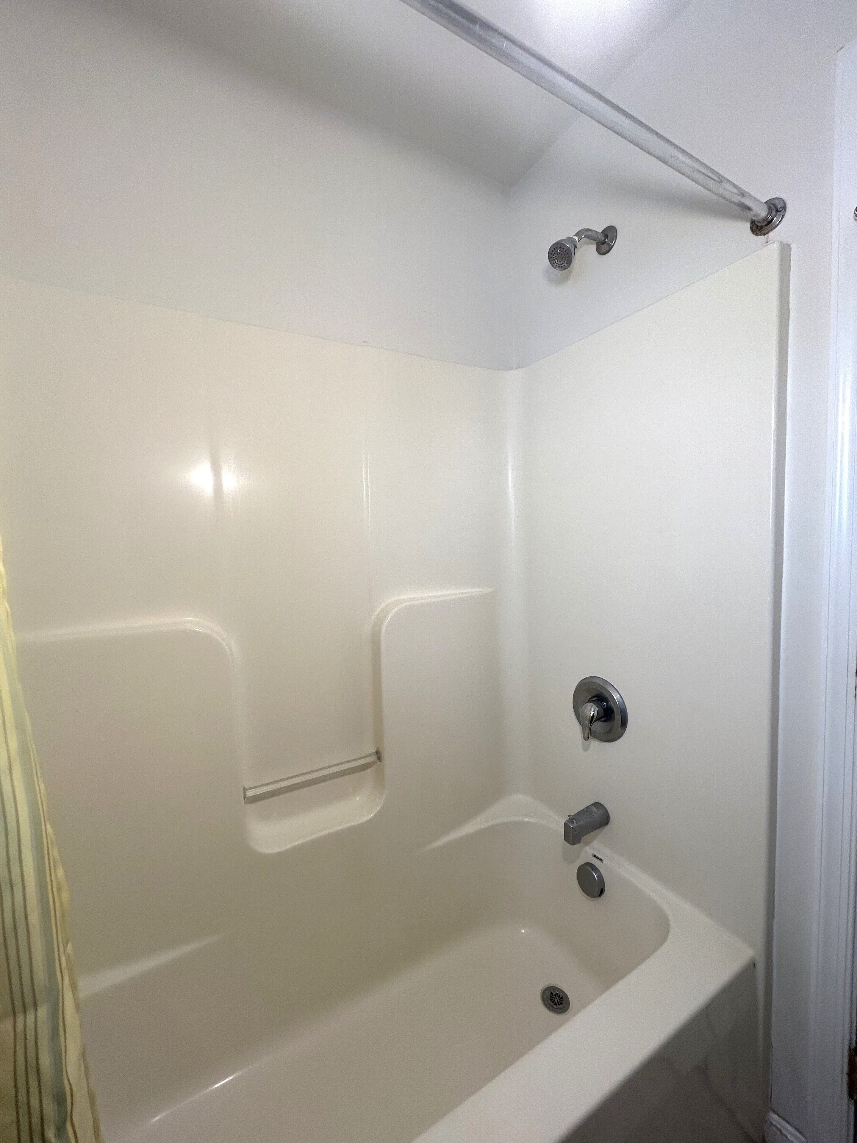 Eine weiße Badewanne mit Duschkopf, Handbrause und einer Haltestange.