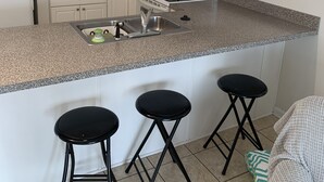 A kitchen with white cabinets, a granite countertop, a stove, a sink, and three black stools.