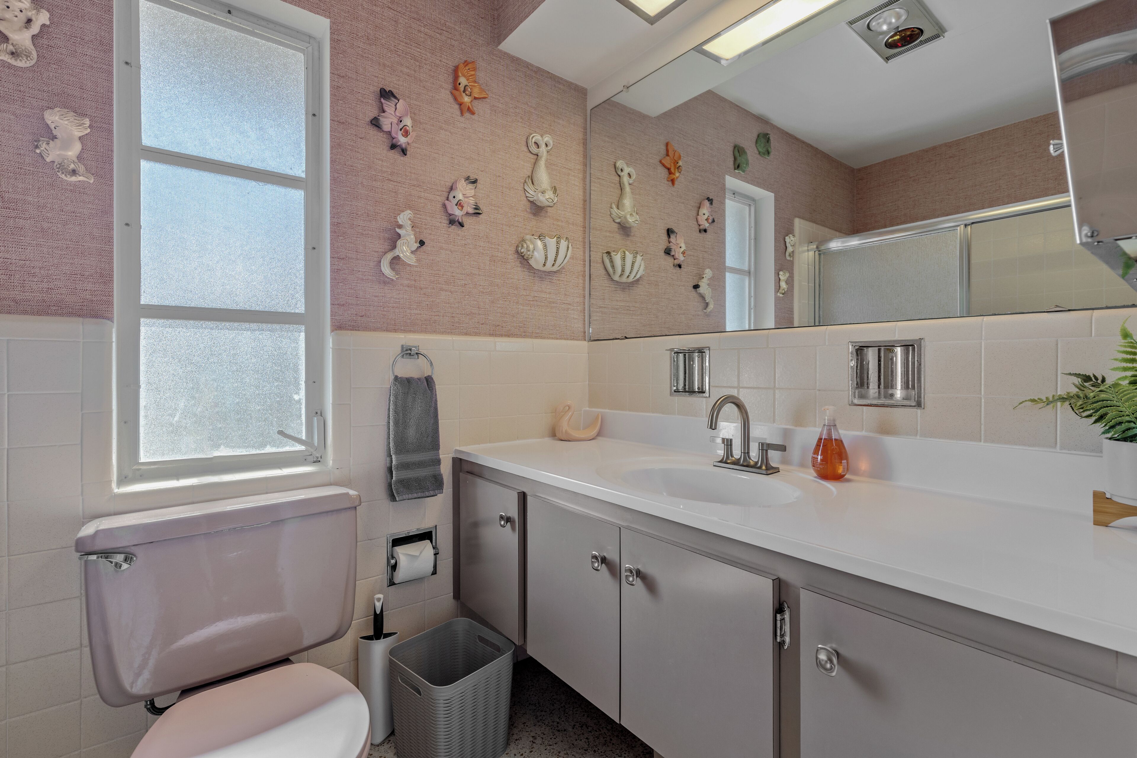 Een badkamer met toilet, wastafel, spiegel en decoratieve muurdecoratie.