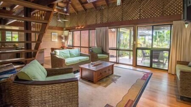 A spacious living area with a high ceiling, large windows, and a view of the outdoors. There are wicker furniture pieces and a coffee table. - Stay at ‘Banfield 3' (Wongaling Beach)