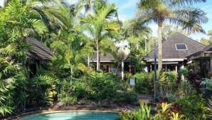 A pool surrounded by lush tropical vegetation and a house with a sloped roof. - Stay at ‘Banfield 3' (Wongaling Beach)