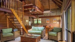 A cozy living room with a wooden staircase, wicker furniture, and a large window. - Stay at ‘Banfield 3' (Wongaling Beach)