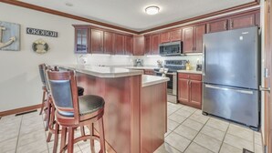 Una cocina con armarios de madera, un refrigerador de acero inoxidable y una barra con taburetes.
