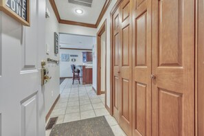 Un pasillo con una puerta de madera, suelo de baldosas y una pequeña cocina al fondo.