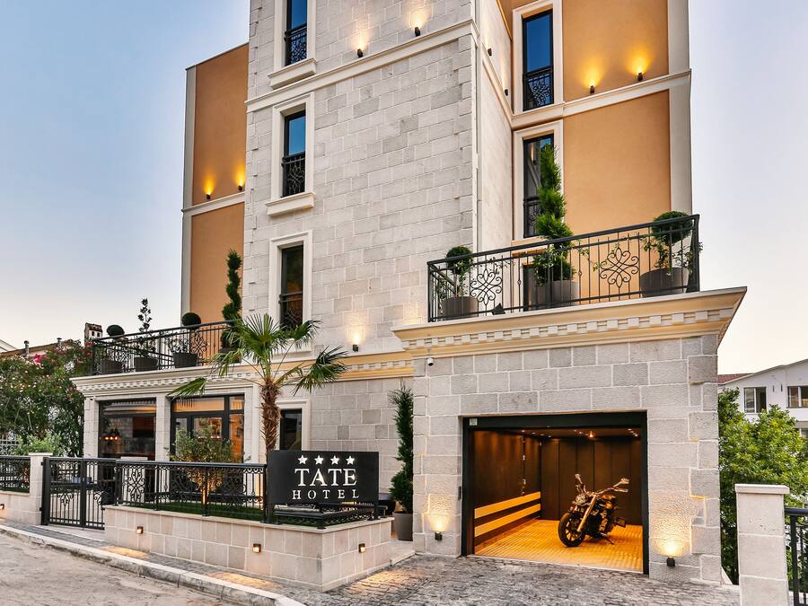 A multi-story hotel with a stone facade, a sign reading "TATE HOTEL", and a motorcycle parked in the driveway.