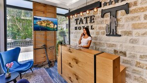 A reception desk with a wooden finish, a large window with a view of greenery, and a wall-mounted sign reading "TATE HOTEL". - Hotel Tate by Aycon (Budva)