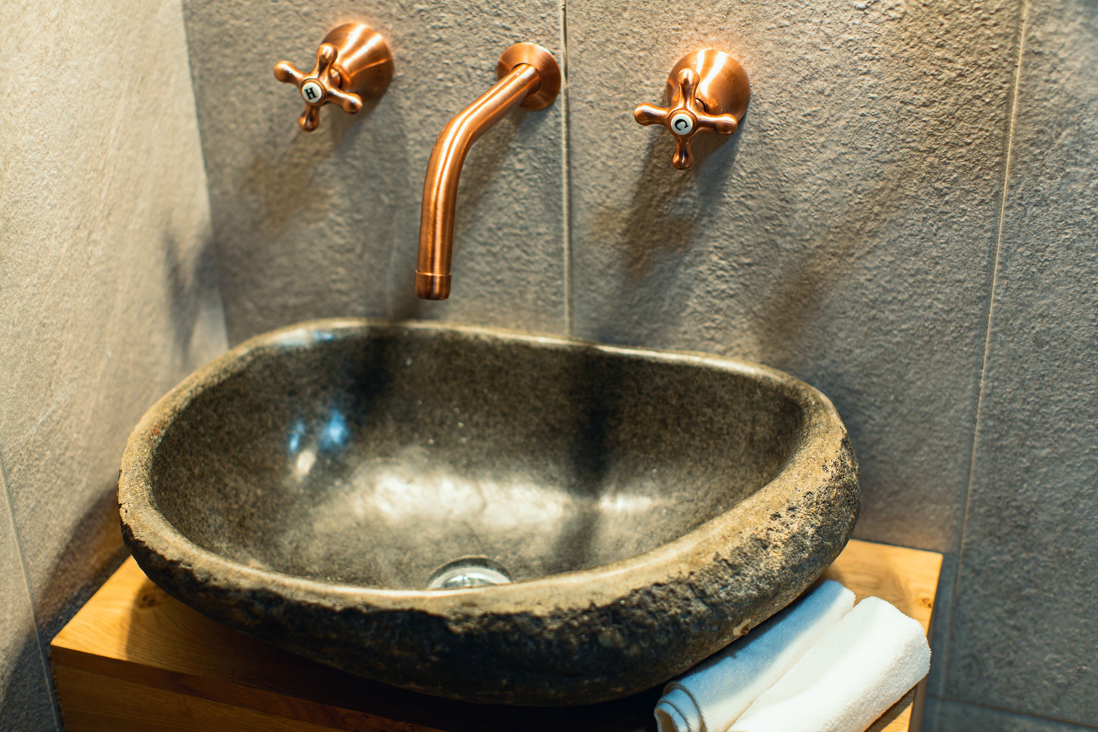 A stone sink with a copper faucet in a bathroom with textured walls.
