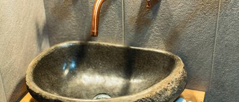A stone sink with a copper faucet in a bathroom with textured walls.
