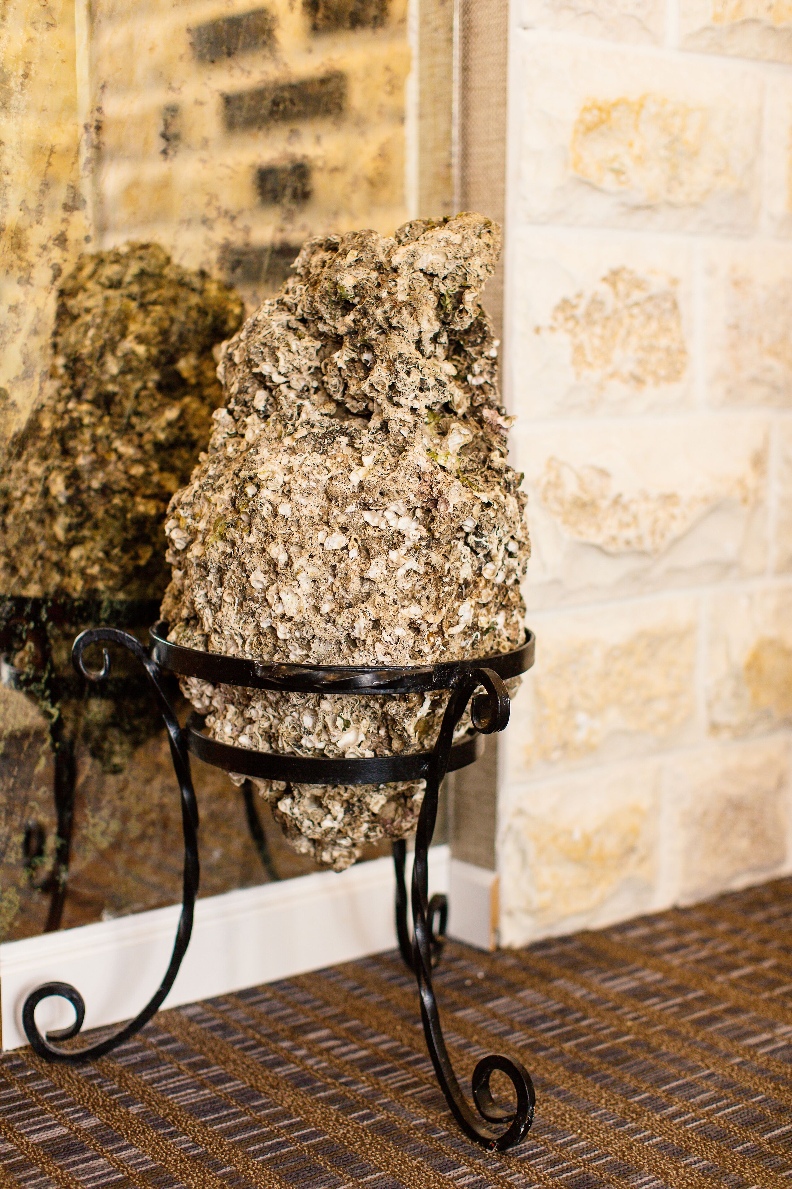 A stone wall with a metal stand holding a large rock.