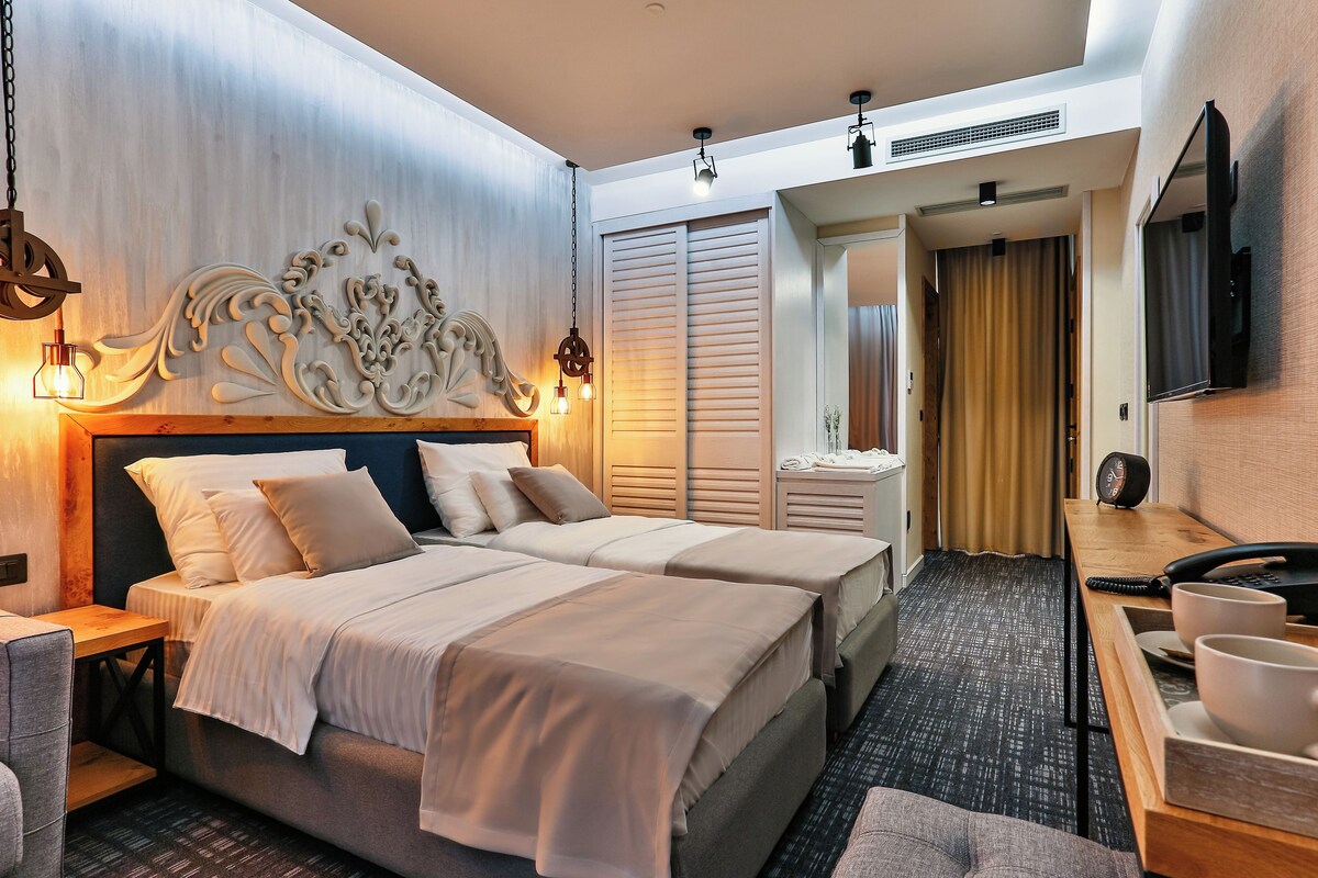 A hotel room with two beds, a wooden headboard, a desk with a telephone, and a television on the wall.