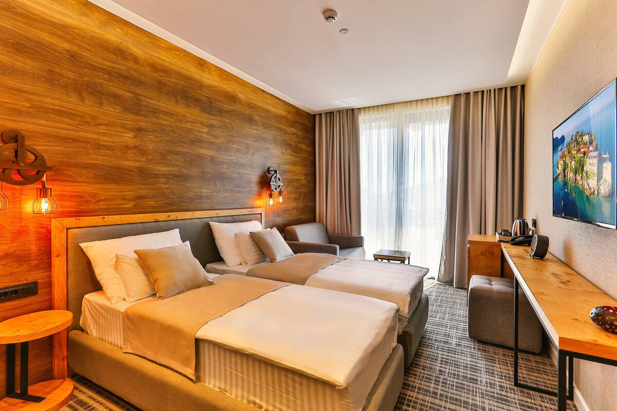 A hotel room with a wooden accent wall, two beds, a desk, a chair, and a TV.
