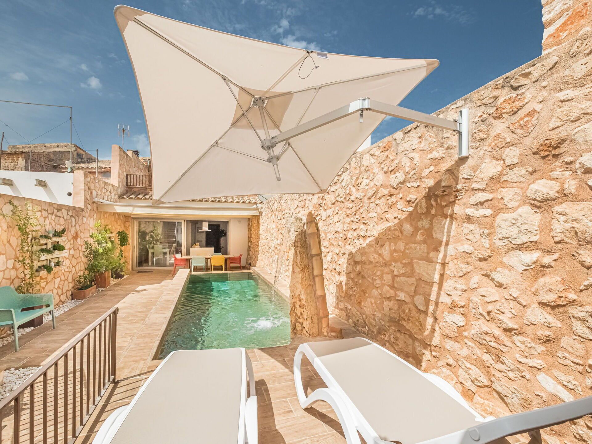Un espace extérieur entouré de murs en pierre, avec une piscine, des chaises longues et une table placée sous un grand parasol.