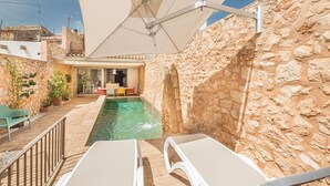 A stone-walled outdoor area with a swimming pool, lounge chairs, and a table under a large umbrella. - Beautiful private villa for 6 guests with WIFI, private pool, TV and terrace (Santanyí)