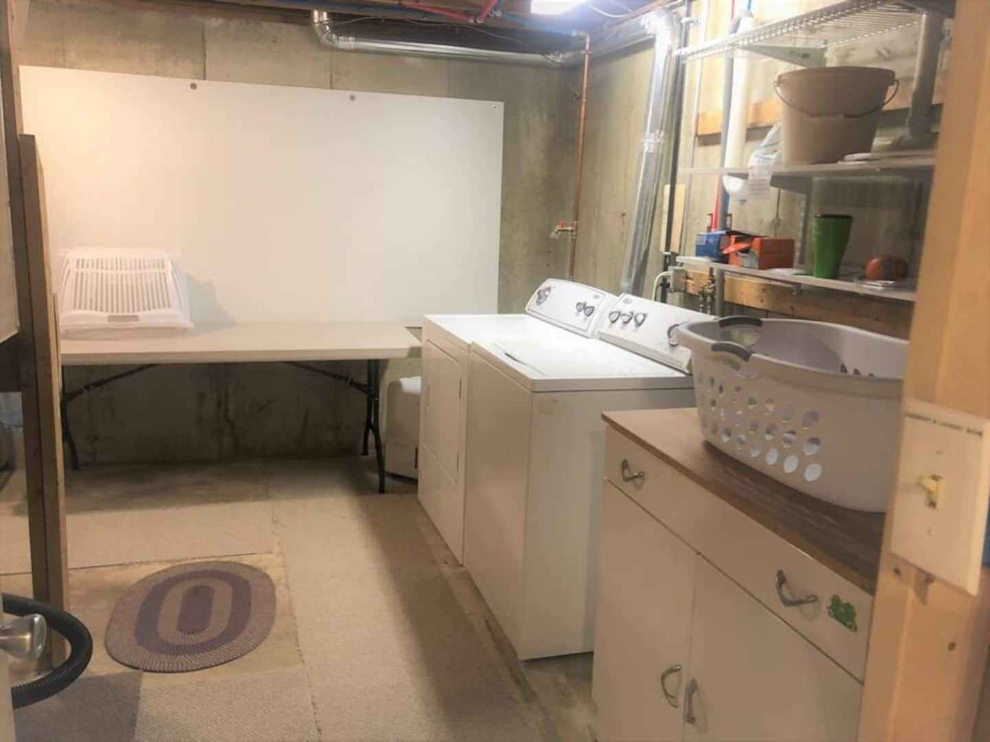 A compact laundry room with a washing machine, dryer, and a small table with a basket.