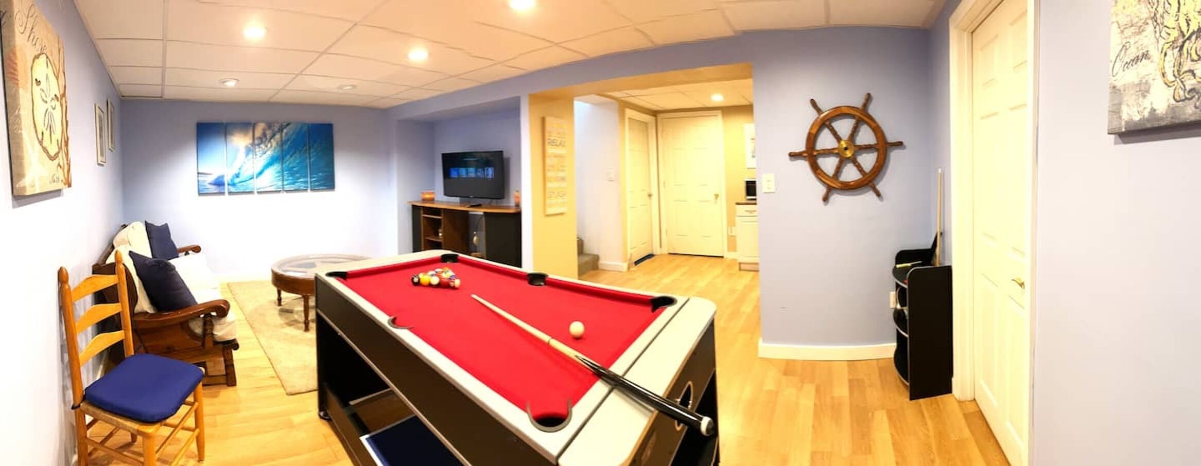 A pool table with a red felt, a television, and a ship's wheel decoration on the wall.