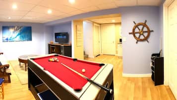 A pool table with a red felt, a television, and a ship's wheel decoration on the wall.