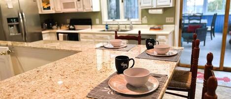 A kitchen with granite countertops, white cabinets, and a dining area with a table set for two.