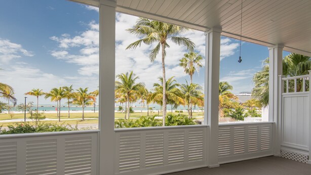 Een overdekte veranda met uitzicht op palmbomen en een strand.
