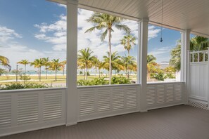 A covered porch with a view of palm trees and a beach.