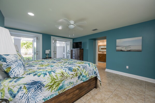 A bedroom with a bed, a ceiling fan, a TV, and a door leading to another room.