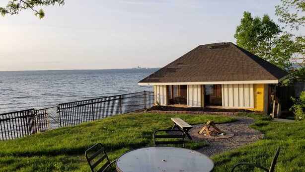 A patio with a table and chairs, a fire pit, and a view of the water.