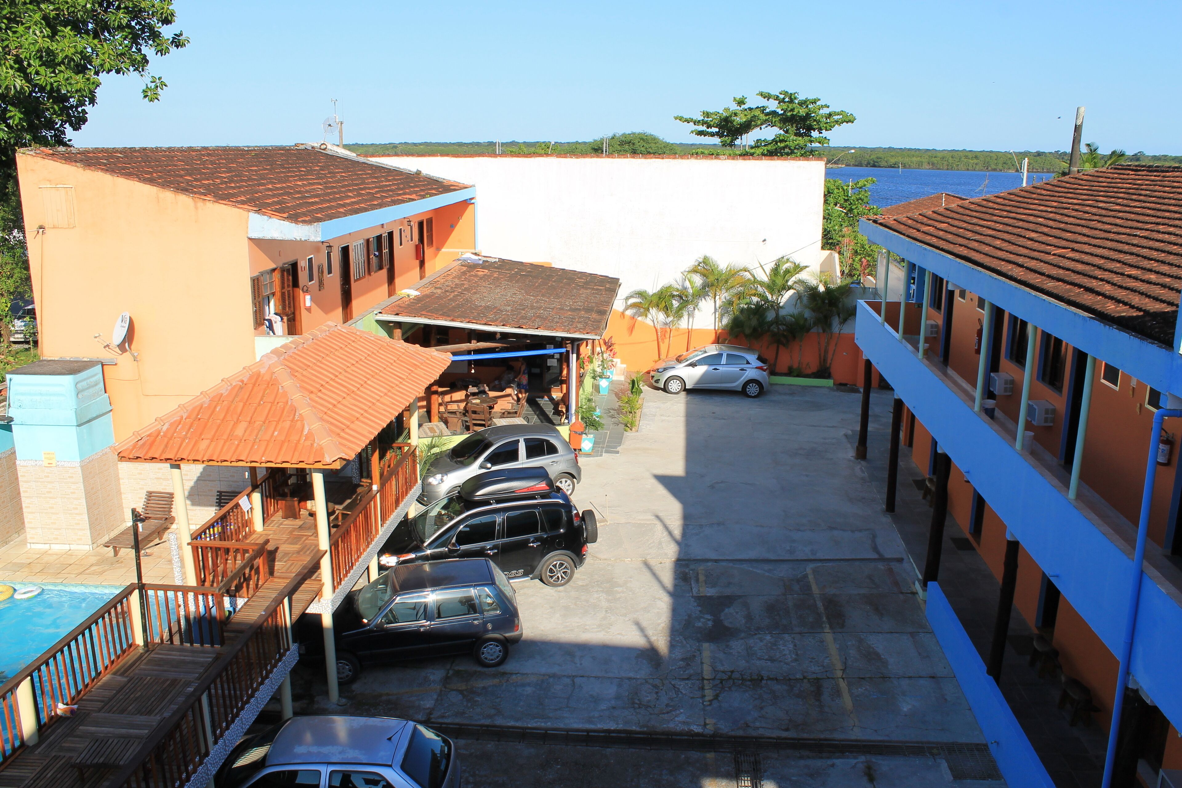 A multi-story building with a swimming pool, parked cars, and a view of the sea.