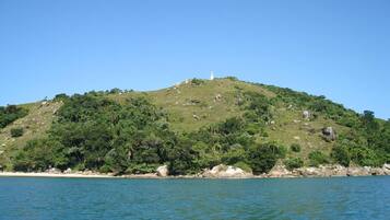 Paisagem costeira com uma colina onde se destaca um farol, rodeada por vegetação densa e um mar calmo.