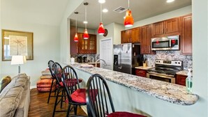 A modern kitchen with a central island, wooden cabinets, stainless steel appliances, and pendant lighting.