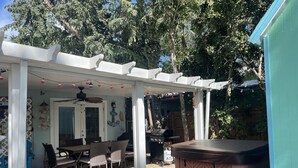 A covered patio with a table and chairs, a hot tub, and a pergola with string lights. - Stay in Paradise (Key Largo)