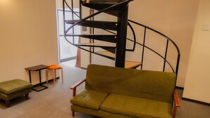 A living room with a green sofa, a small table, a stool, and a spiral staircase. - bnb+ Namba - Hostel (Osaka)