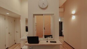 A hotel room with a desk, a laptop, a clock, and a window. - bnb+ Namba - Hostel (Osaka)