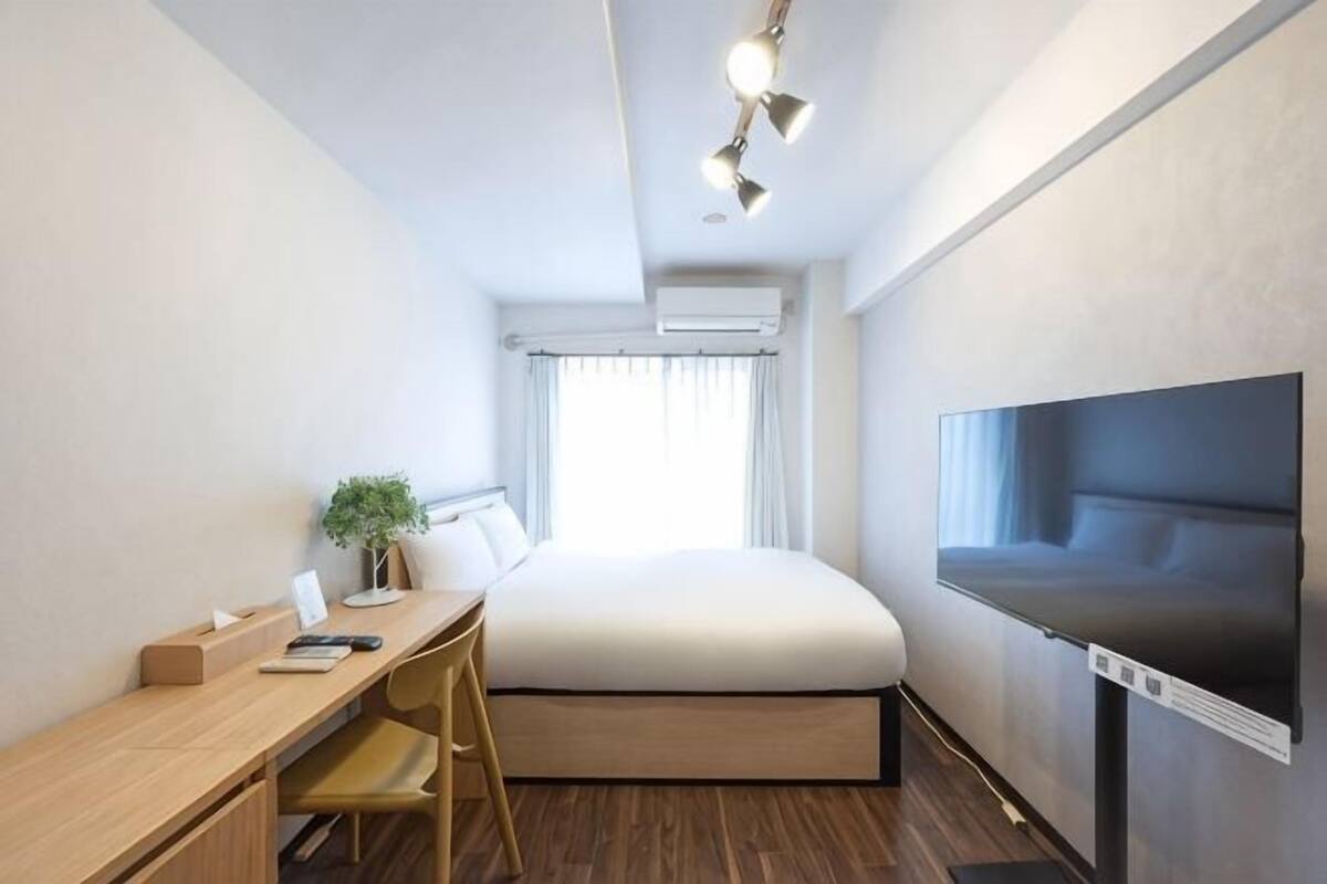 Habitación de hotel compacta con cama, escritorio, silla y televisor montado.