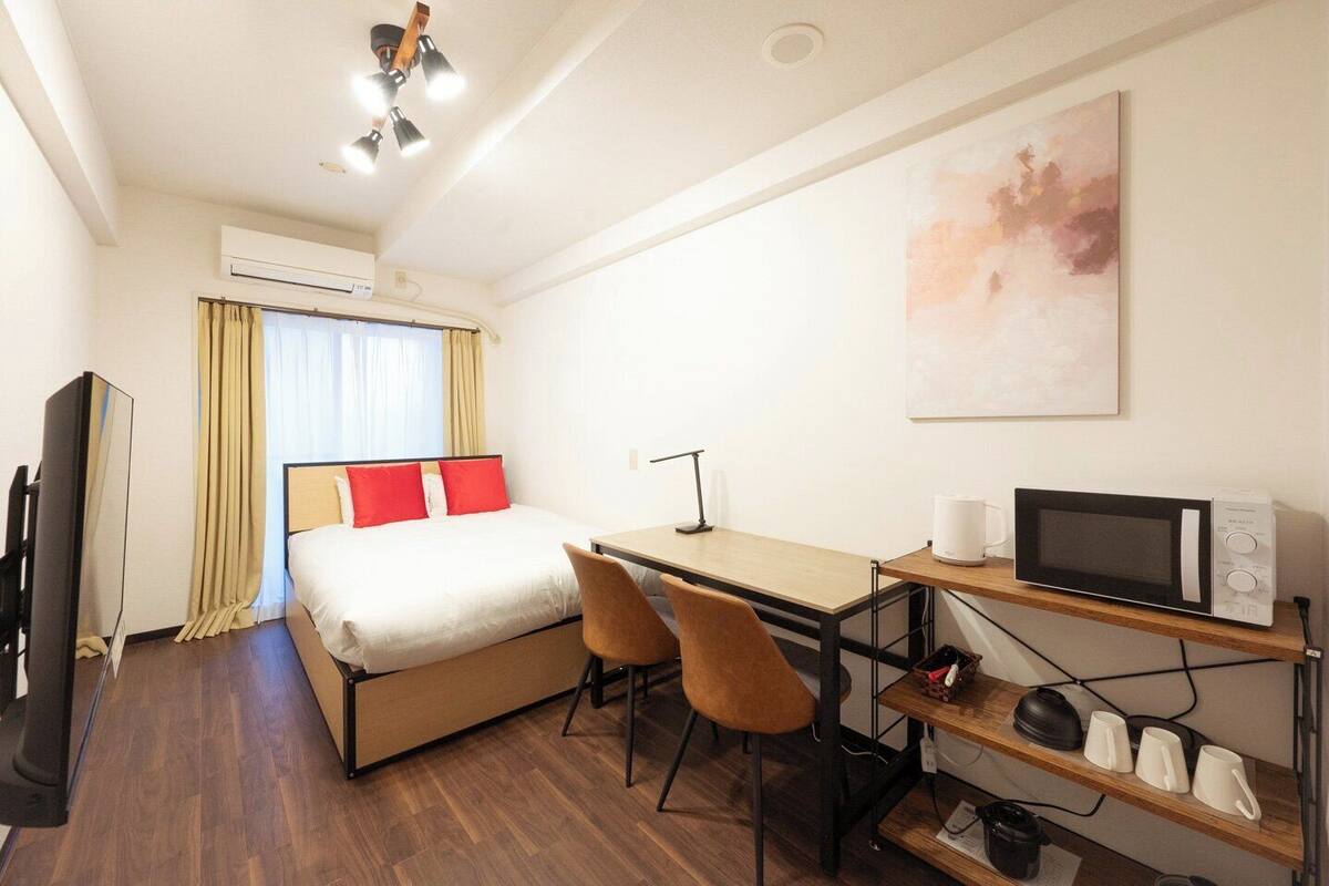 Habitación de hotel con cama, escritorio, sillas, televisor, microondas y un cuadro en la pared.