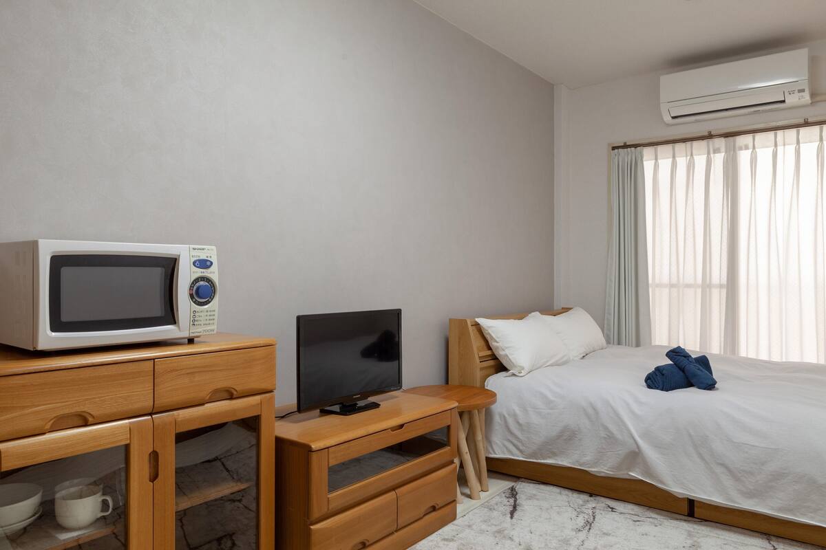 Habitación de hotel con escritorio de madera, televisor, cama con ropa de cama blanca y equipo de aire acondicionado.