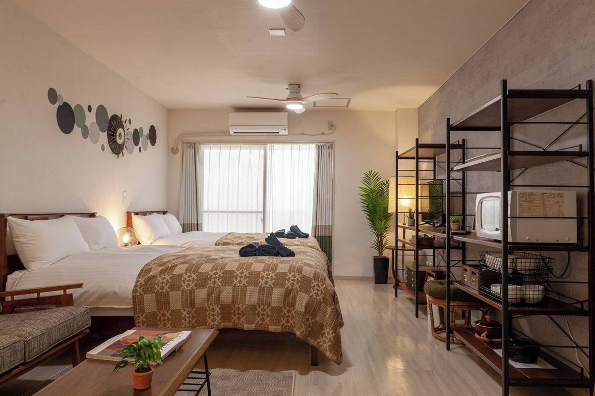 Una habitación de hotel con dos camas, un escritorio, una estantería y una ventana con cortinas.