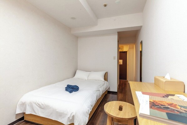 A small, clean room with a single bed, a wooden table, and a small stool. - ELM Takadanobaba (Tokyo)
