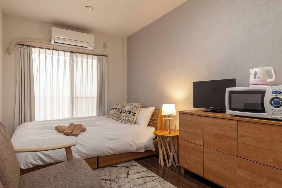 Habitación de hotel con cama, televisor, microondas, una mesita de noche con lámpara y sofá.