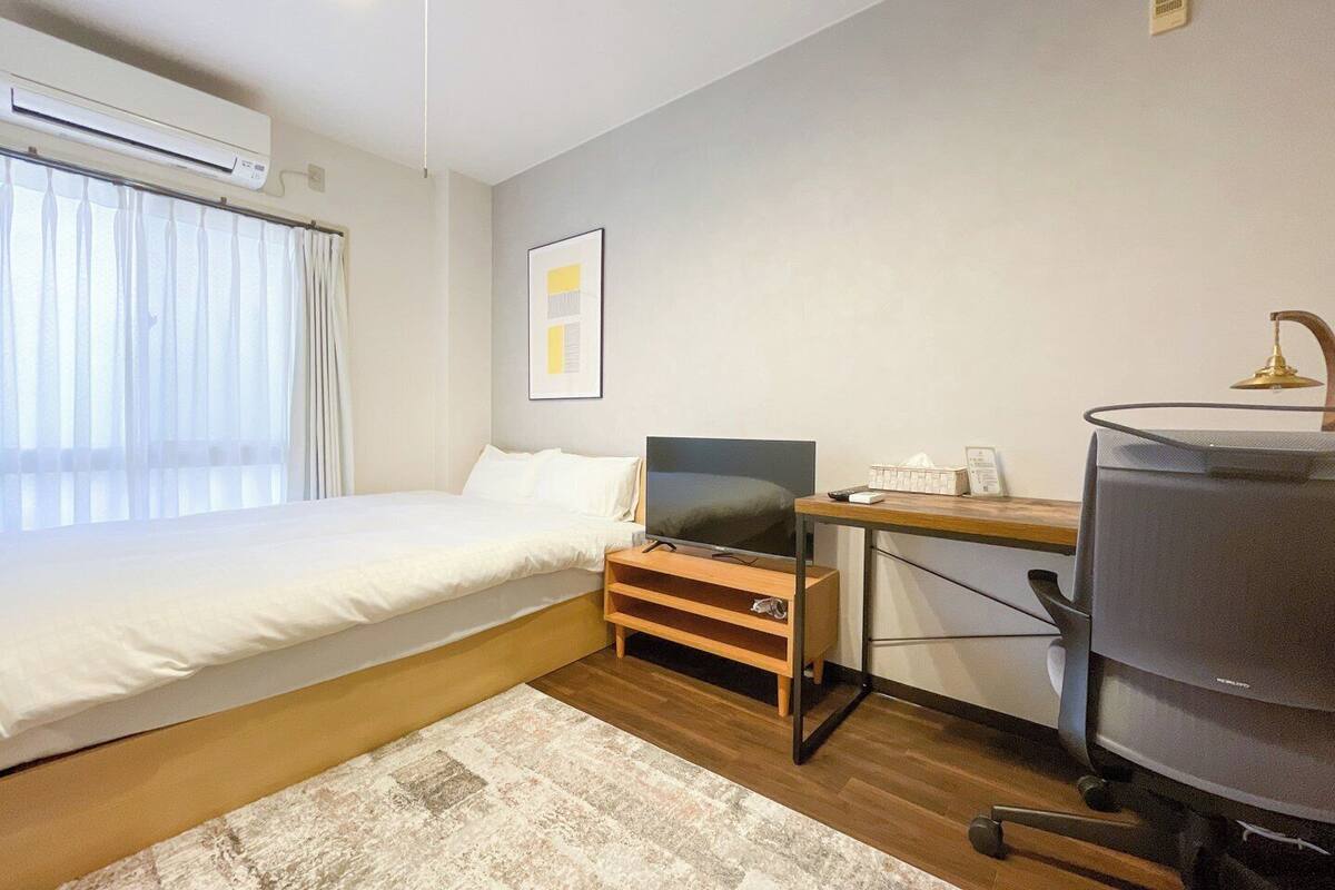 Un dormitorio con cama, escritorio, silla, televisor y aire acondicionado.