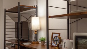 Un espacio de trabajo con un escritorio, estanterías, una lámpara, un reloj, una planta y una tetera.