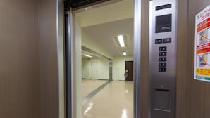 Interior de un ascensor con panel de control, señal de salida de emergencia y un pasillo que lleva a una puerta.