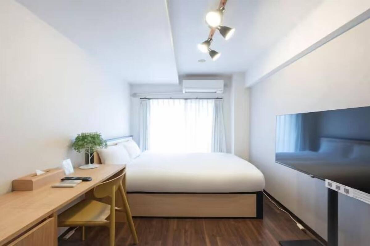 Habitación de hotel pequeña con cama, escritorio, silla y un ventanal grande.
