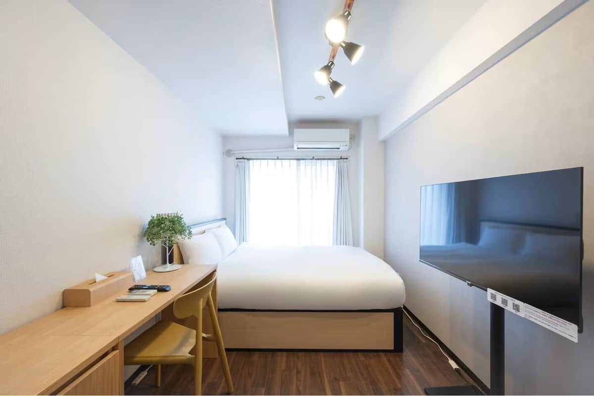 Habitación de hotel moderna con cama, escritorio, silla, televisor y planta.