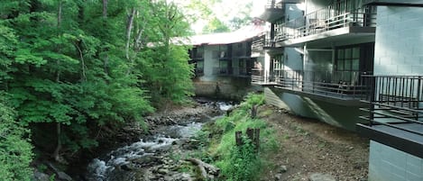 A building with a stone facade, a balcony, and a view of a flowing river surrounded by dense greenery.