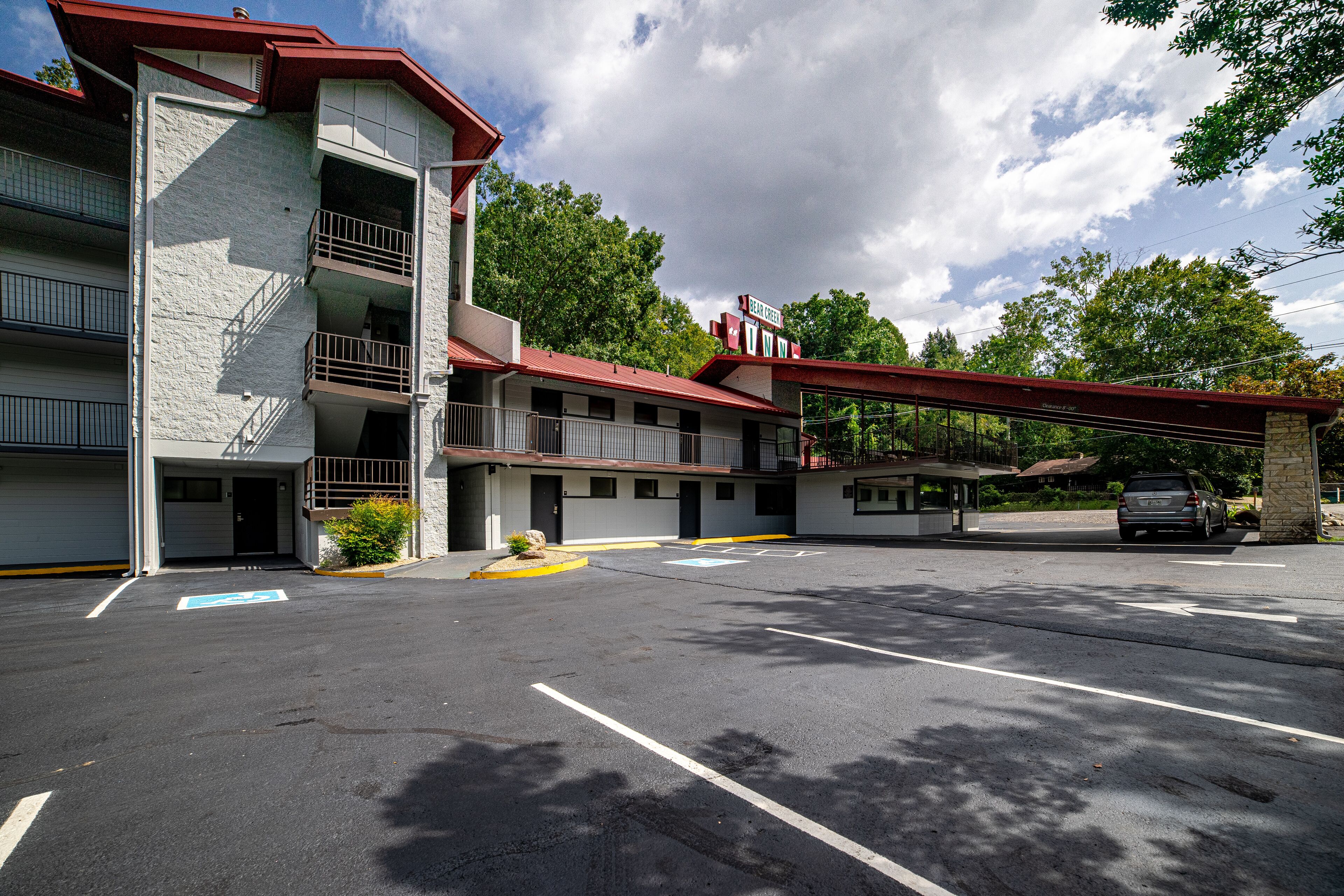 A multi-story motel with a red roof and white exterior walls, featuring a parking lot with marked handicapped spaces.