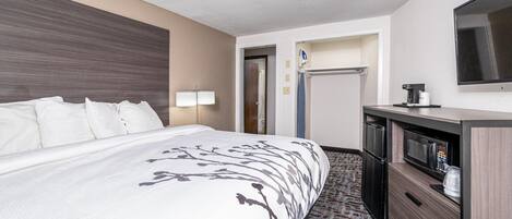 Una habitación de hotel con una cama grande, un escritorio con microondas y un televisor en la pared.