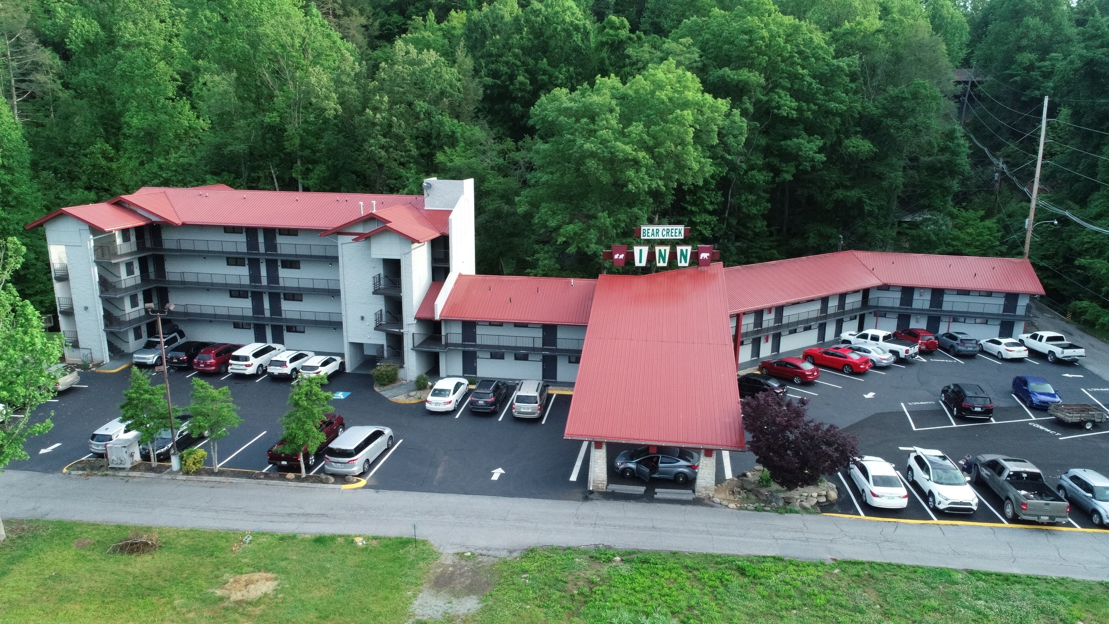 Um edifício de vários andares com telhado vermelho, estacionamento e uma placa com a inscrição 'Bear Creek Inn'.