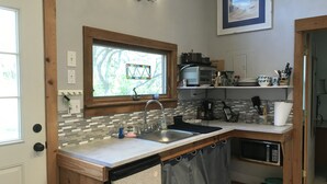 Eine kleine Küche mit Fenster, Spüle, Mikrowelle und Geschirrgestell.