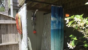 Eine Holzdachterrasse mit Duschbereich, einer hängenden Duschbrause und einem blauen Duschvorhang.