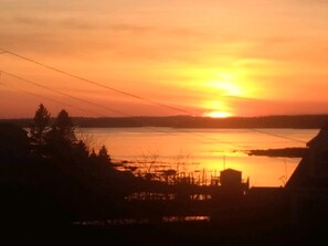 A sunset over a body of water with silhouettes of trees and buildings.