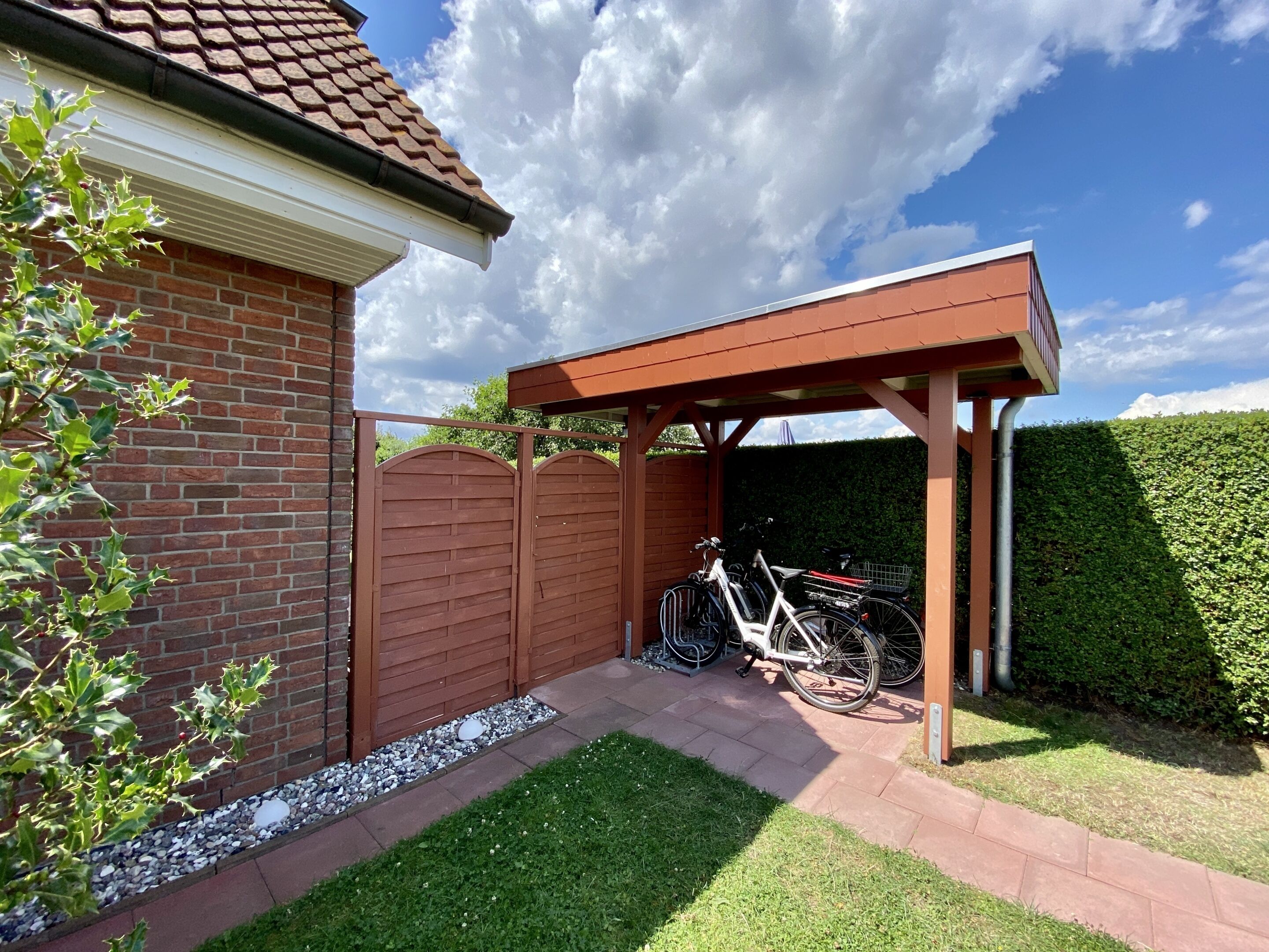 A brick house with a covered patio, a hedge, and a bicycle parked outside.